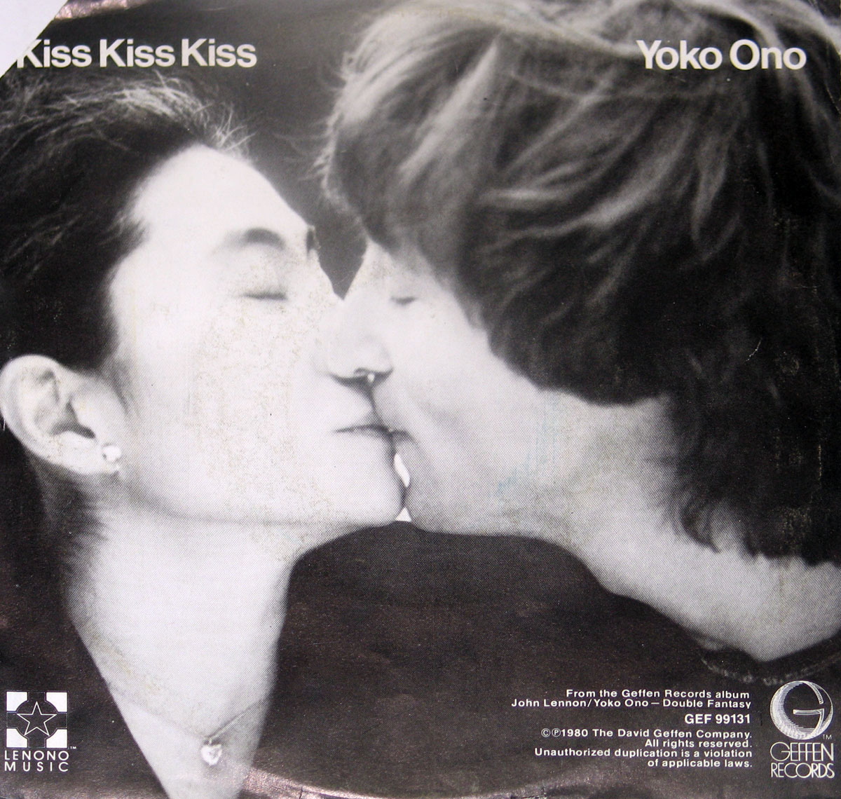 Black and white cover art of Yoko Ono’s ‘Kiss Kiss Kiss’ single, featuring an intimate close-up of Yoko Ono and John Lennon kissing. Yoko's face is turned slightly leftward, her eyes closed, wearing a heart-shaped pendant and pearl earrings. Lennon’s face is angled toward her, eyes closed, with tousled hair. The text ‘Kiss Kiss Kiss’ and ‘Yoko Ono’ appear in the top corners, with logos for Lenono Music and Geffen Records at the bottom. Additional copyright and album information is present.